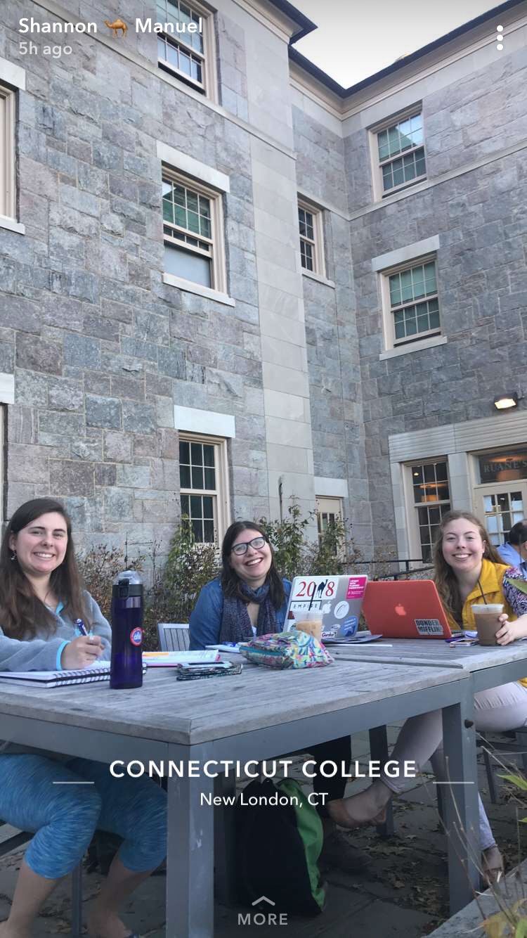 Julia and two other female students sit at tables outside of the Ruane's Den Coffee Closet doing school work. 
