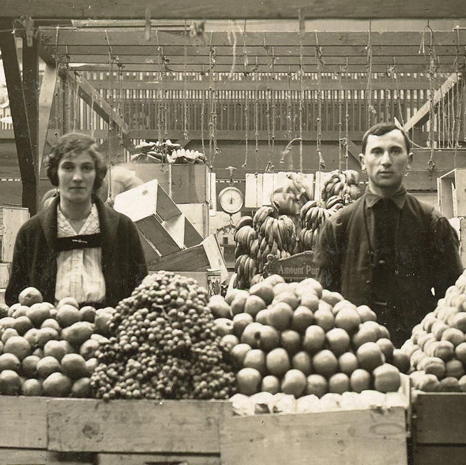 Historic image of early 20th century couple behind a fruit stand