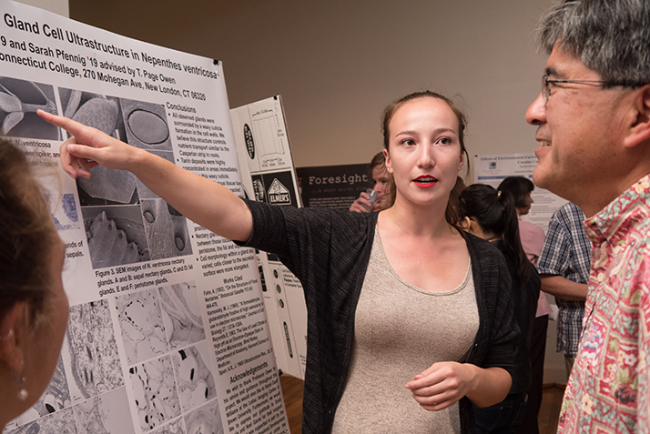 A student points to her poster to explain her research to a professor. 