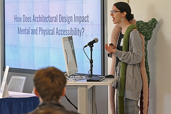 Beth Marsh ’24 wears an anxiety-reducing weighted “sensory squid” she created as she presents her research, “Designing for Disability Justice: How Does Architecture Impact Mental and Physical Accessibility.”