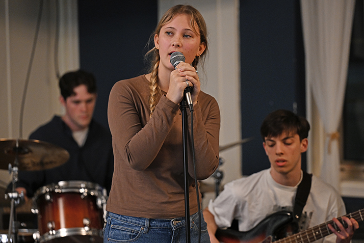 A singer at the microphone with guitarist and drummer behind her